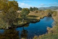 Bright blue winding river flows in grass, bushes, trees among the mountains and blue sky with clouds. Reflections in the water. Royalty Free Stock Photo