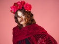 A bright and bold young woman with roses on her head and a red knitted cape.