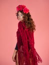 A bright and bold young woman with roses on her head and a red knitted cape.