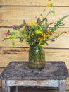 A bright bouquet of wildflowers of yellow and violet shades in a glass jar on an old stool on the porch of a nesting house
