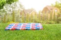 Bright checkered mat on green grass lawn under trees in garden. Blurred wooden houses on background. Empty space for Royalty Free Stock Photo