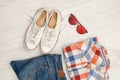 Bright checkered shirt, glasses, sneakers and jeans. Wooden background. Fashionable concept