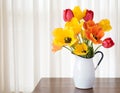 Bright and Cheerful Spring Tulip Bouquet in a White Metal Vase on dark wood and against White Curtain Background