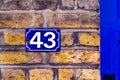 House number 43 on a blue email sign on a brick wall next to a blue front door
