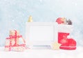 Bright christmas mock up with white photo frame: festive gift boxes, toys, and fir-cones in red santa`s boot under snow. New year Royalty Free Stock Photo