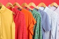 Bright clothes on hangers against red, closeup. Rainbow colors