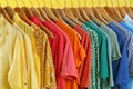 Bright clothes on hangers against yellow, closeup. Rainbow colors