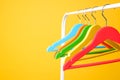 Bright clothes hangers on metal rack against yellow background, closeup. Space for text Royalty Free Stock Photo