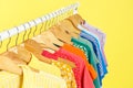 Bright clothes hanging on rack against yellow, closeup. Rainbow colors