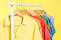 Bright clothes hanging on rack against yellow, closeup. Rainbow colors