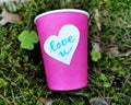 Bright coffee cup with sticker Love U in grass. Heart shape sticker with lettering. Paper cup on nature background. Love coffee ou Royalty Free Stock Photo