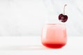 Bright cold layered cherry cocktail with liqueur, slice cherry in modern minimal soft light white bar interior.
