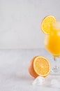 Bright cold summer tropical alcohol orange cocktail of ripe oranges and ice cubes in elegance misted wineglass white wood board.