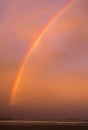 Bright colorful double rainbow during sunset with gloomy blurred red shimmering sky over the ocean