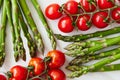 Bright and colorful flat lay composition of asparagus stems and branches of cherry tomatoes on a white rustic table.