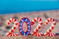 Bright, colorful, funny striped numbers of 2022 against the background of a sandy beach and the sea. Creative Christmas card. Royalty Free Stock Photo