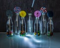 Bright and colorful lollipop and candies in bottles standing on the glass table in the dark on background of lines of light. Royalty Free Stock Photo