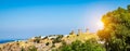 Panoramic landscape view of Patmos Island at sunset with three windmills on the hill against blue sky background on a summer day.