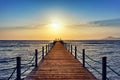 Bright and colorful sunrise over the sea and pier. Perspective view of wooden pier on the sea at sunrise with rocky Royalty Free Stock Photo