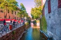 Bright colors of Annecy, France. Tourists walk across the street near green channel