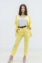 Confident brunette girl holding hands in pockets of bright stylish yellow suit and posing in studio on white background. Royalty Free Stock Photo