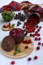 Bright composition of a ceramic mug with raspberries on a wooden board and a bowl with red hawthorn berries on a light wooden