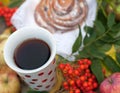 A A bright composition with a cup of strong black tea, a sweet bun with raisins, ash berries, apples and colorful autumn leaves on Royalty Free Stock Photo