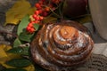 A A bright composition with a cup of strong black tea, a sweet bun with raisins, ash berries, apples and colorful autumn leaves on Royalty Free Stock Photo