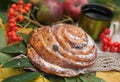 A bright composition with a cup of strong black tea, sweet bun with raisins, ash berries, apples and colorful autumn leaves on a Royalty Free Stock Photo