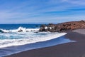 The bright contrast of the white sea foam of the waves rolling onto the shore with the sand and black solidified lava Royalty Free Stock Photo