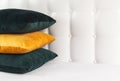 Bright decorative soft pillows in bed on the background of leather quilted headboard. Emerald and orange pillow, part of bed close