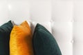 Bright decorative soft pillows in bed on the background of leather quilted headboard. Emerald and orange pillow, part of bed close