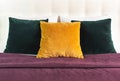 Bright decorative soft pillows in bed on the background of leather quilted headboard. Emerald and orange pillow, part of bed close