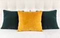 Bright decorative soft pillows in bed on the background of leather quilted headboard. Emerald and orange pillow, part of bed close