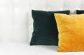 Bright decorative soft pillows in bed on the background of leather quilted headboard. Emerald and orange pillow, part of bed close