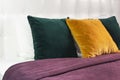 Bright decorative soft pillows in bed on the background of leather quilted headboard. Emerald and orange pillow, part of bed close