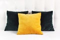 Bright decorative soft pillows in bed on the background of leather quilted headboard. Emerald and orange pillow, part of bed close