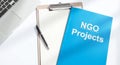 A bright desk scene featuring a laptop, clipboard, pen, and a blue ngo projects folder on a white surface Royalty Free Stock Photo
