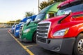 Bright different big rigs semi trucks standing in row on truck stop parking lot