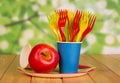 Bright disposable tableware and apple on abstract green background.