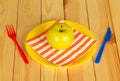 Bright disposable tableware, napkin and apple on background light wood.