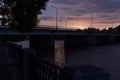 Bright dramatic summer background - sunset on river with black silhouette bridge, lanterns, wonderful sky in golden, pink, purple.