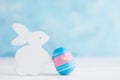 Bright Easter background: white wooden bunny with paited egg against blue wall. Holiday concept