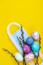 Bright Easter eggs, medical masks, willow branches on colored background. Quarantine Easter. Stop COVID-19 VIRUS