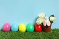 Bright Easter eggs, pot with flowers and toy bunny on green grass against light blue background Royalty Free Stock Photo