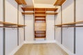 Bright empty walk-in closet with wood shelves, beige carpet floor. Royalty Free Stock Photo