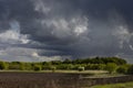 Bright epic thunderstorm landscape in early spring with dark blue fluffy clouds in sunlights above black field arable land. Royalty Free Stock Photo