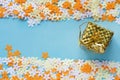 Bright festive background or backdrop of multi-colored confetti flowers and a golden box with a gift on a blue background. Royalty Free Stock Photo