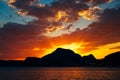 Bright fiery sunset behind the silhouette of a mountain over the sea.