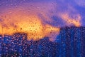 Bright fiery sunset through raindrops on window with bokeh lights. Abstract background. Water drop on the glass against the